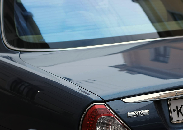 Close-up of a car's rear, featuring a sleek, reflective surface with building reflections and partial view of a license...